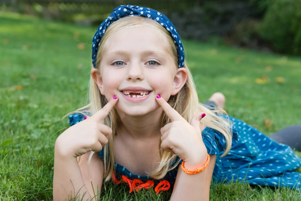 Young girl smiling and pointing to spaces left by missing baby teeth.