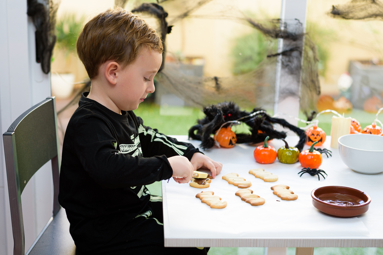 Child preparing Halloween cookies with chocolate frosting at home.